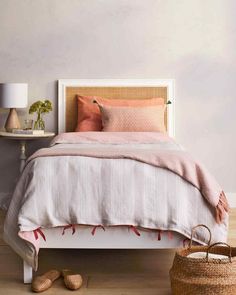 a white bed with pink and orange pillows in a bedroom next to a wicker basket