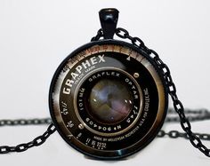 a camera lens necklace is shown on a white surface with chain attached to the pendant