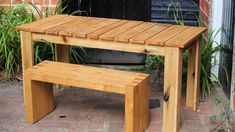 a wooden table and bench in front of a brick wall