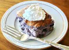 a piece of cake with whipped cream on top sits on a plate next to a fork