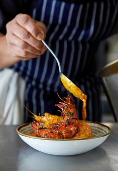 a person in an apron is holding a spoon over a bowl of food with shrimp on it