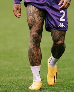 a man with tattoos on his legs and yellow shoes is standing in the grass while wearing soccer cleats