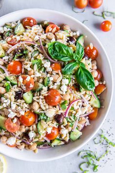 a white bowl filled with rice salad next to sliced lemons and fresh basil leaves