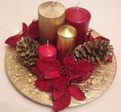 three candles are sitting on a gold plate with red poinsettias and pine cones