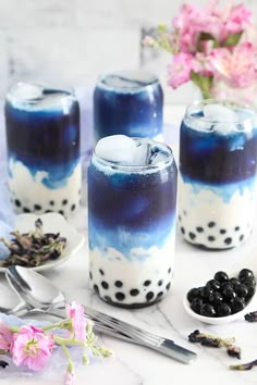 blue and white drinks with blackberries in them on a marble counter top next to flowers