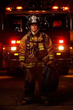 a fireman standing in front of a fire truck with his helmet on and holding a large object