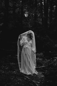 a woman in a white dress standing in the woods wearing a veil over her head