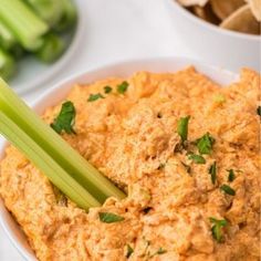 celery sticks sticking out of a dip in a white bowl next to chips