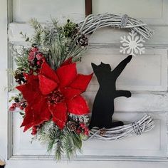 a christmas wreath with a cat and poinsettis on it, sitting next to a door