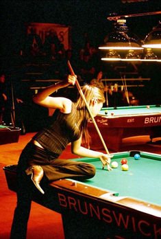 a woman is playing pool in a dark room