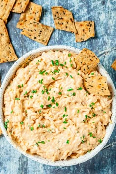 a bowl filled with dip and crackers on top of a blue table next to chips