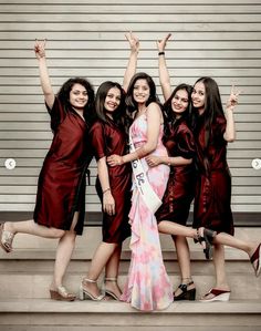 a group of women standing next to each other in front of a wall holding their hands up