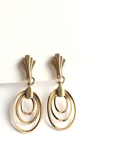 Stunning gold filled vintage earrings from the Retro period have a concentric oval hoops of square wire beneath retro fan flourishes at the ear. Really great looking worn with fitted clothing of the 40s and 50s. Length is 1.6 inches. Width is 0.6 inches. Screw back 12K gold filled earrings are made by and signed Krementz. International shoppers are responsible for all customs and import fees at checkout or upon delivery. Priority shipping upgrades available. We gift box all our jewelry. Need you Retro Yellow Gold Earrings, Vintage Oval Earrings With Lever Back Ear Wires, Vintage Oval Metal Earrings, Gold Retro Hoop Jewelry, Retro Gold Hoop Jewelry, Retro Oval Earrings For Formal Occasions, Retro Gold Oval Earrings, Retro Yellow Gold Metal Earrings, Retro Yellow Gold Clip-on Earrings