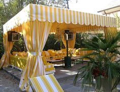 a yellow and white striped tent set up for an outdoor event with lounge chairs and tables