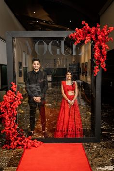 a man and woman standing in front of a window with red flowers on the floor