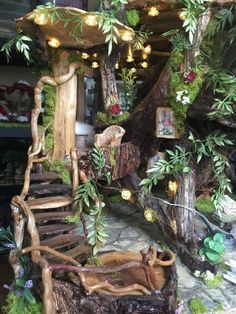 a fake tree house made out of logs and branches with lights on the top, surrounded by greenery