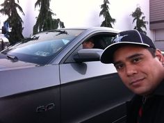 a man sitting in the drivers seat of a car next to a parked black car