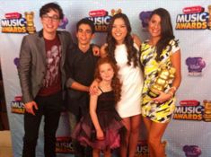 a group of people standing next to each other in front of a wall with music awards on it