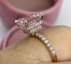 a woman's hand holding an engagement ring with a pink diamond in the center