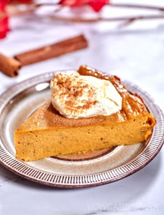 a slice of pumpkin pie on a plate with whipped cream and cinnamon sticks in the background