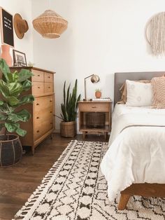 a bedroom with a bed, dresser and plants on the side table in front of it