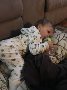 a small child laying on top of a couch drinking from a water bottle in his mouth