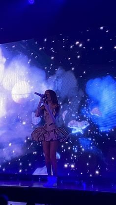 a woman standing on top of a stage in front of a large screen holding a microphone