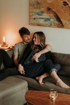 a man and woman sitting on a couch in front of a table next to a lamp