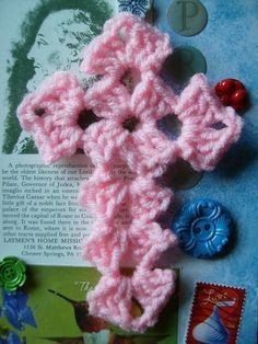 a crocheted pink cross is sitting on top of an open book with buttons