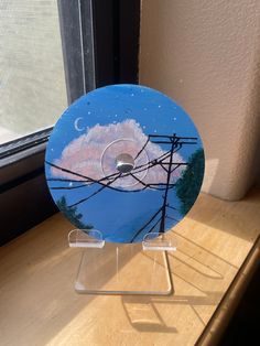 a cd sitting on top of a wooden table next to a window with a sky and clouds painted on it