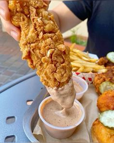 a person is dipping some food into a small bowl with sauce on it and fries in the background