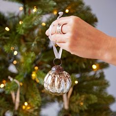 a hand holding a glass ornament in front of a christmas tree