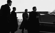 three men are standing in front of a car near an airplane on the tarmac