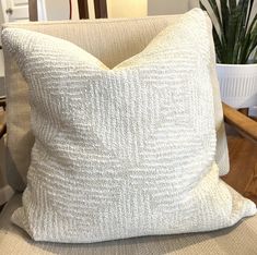 a white pillow sitting on top of a chair next to a potted green plant