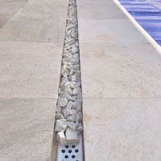 a row of rocks sitting on top of a sidewalk next to a swimming pool with water