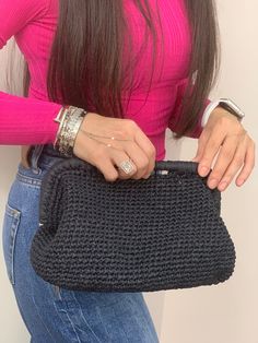 a woman holding a black crochet purse in her right hand and wearing a pink shirt