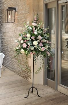 a tall vase with flowers on a stand in front of a brick wall and door