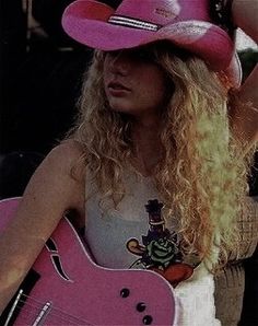 a woman wearing a pink cowboy hat and holding a pink guitar in her right hand