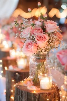 pink roses and baby's breath in a mason jar on a table with candles