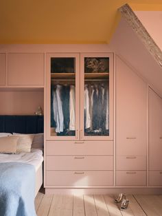 an attic bedroom with pink walls and wooden flooring, built - in wardrobes