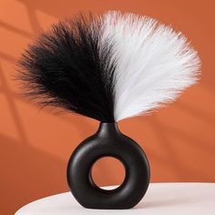 a black vase with a white and black feather on the top is sitting on a table