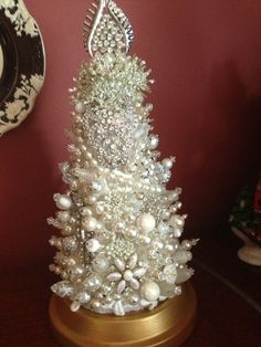 a small white christmas tree with pearls and other ornaments on a table next to a plate