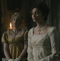 two women standing next to each other in front of a lit candle on a table