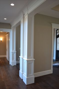 an empty room with white columns and hard wood flooring