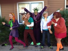 group of people dressed in costumes posing for the camera outside their house with one person holding his arms out