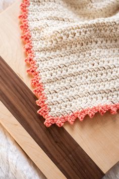 an orange and white crocheted blanket sitting on top of a wooden cutting board