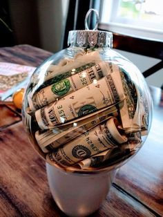 a glass ornament filled with money sitting on top of a wooden table