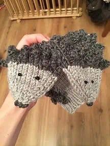 someone is holding two knitted sheep mitts