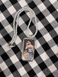 a necklace with an image of a woman on the front and back of it, sitting on a black and white checkered table cloth