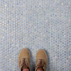 a person standing on a tiled floor with their feet in the air and wearing brown shoes